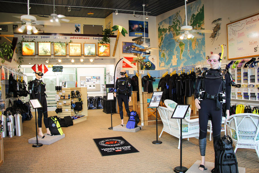 A shot of the scuba store from the entrance. Mannequins are set up to display 3 different scuba systems and shelves display the scuba and snorkeling equipment. 