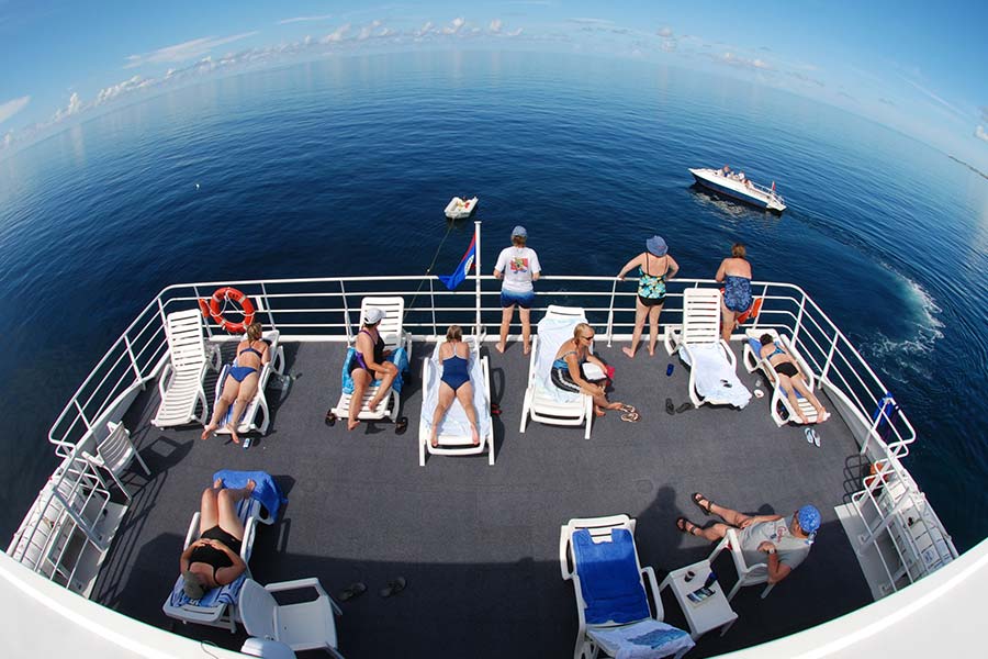 The Aqua Cat sundeck hosts several seats with people laying in the sun, reading, or watching the water.