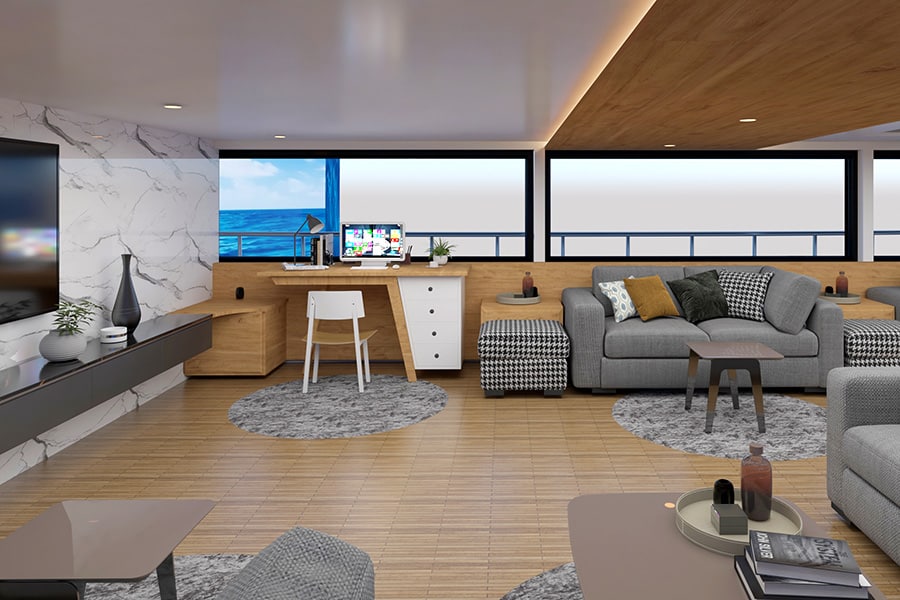 One of the rooms aboard the liveaboard is shown with couches and desks, and is covered with large windows in the background. 