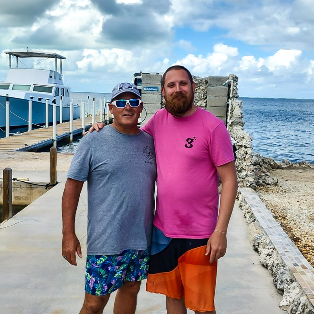Billy and Capt Steve Burner are standing on the Quiescence dock in Key Largo. Both are wearing Gypsy Divers shirts and smiling at the camera. 