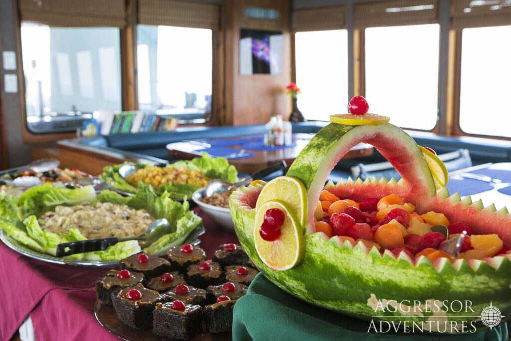 The buffet table on the Belize Aggressor IV is loaded with various foods. A fruit basket with fresh fruit, and several types of salads. 