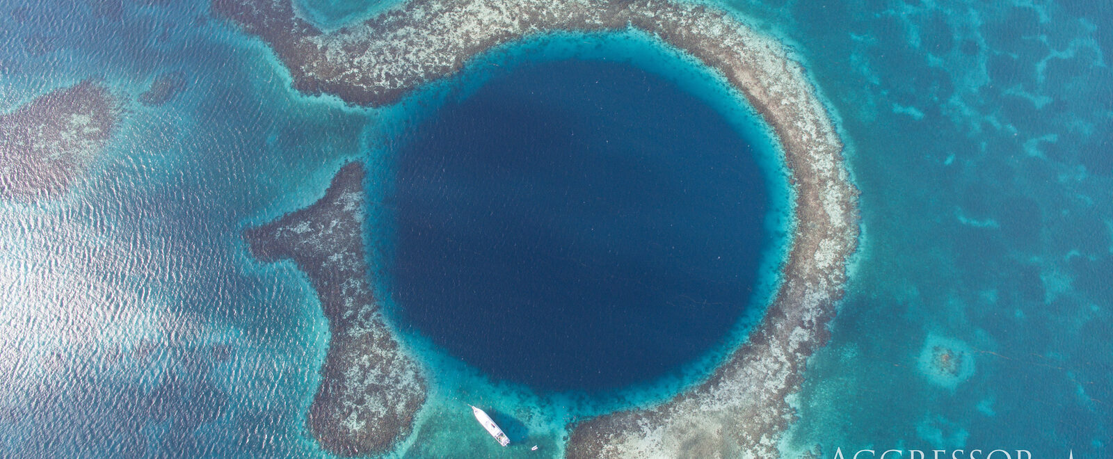 A blue hole is seen below in the ocean. The hole is a much darker color than the rest of the ocean and is perfectly round.